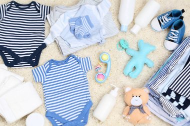 Baby clothes with toys and diapers on carpet clipart