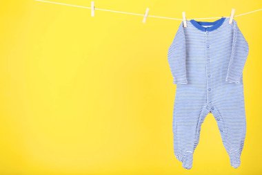 Bebek kıyafetleri sarı arka planda asılı.