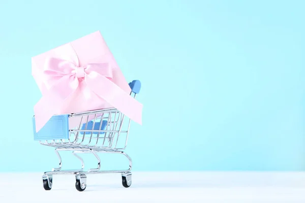 Pequeno carrinho de compras com caixa de presente em fundo azul — Fotografia de Stock