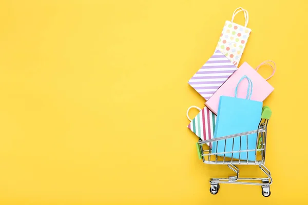 Pequeño carro de metal con bolsas de compras sobre fondo amarillo —  Fotos de Stock