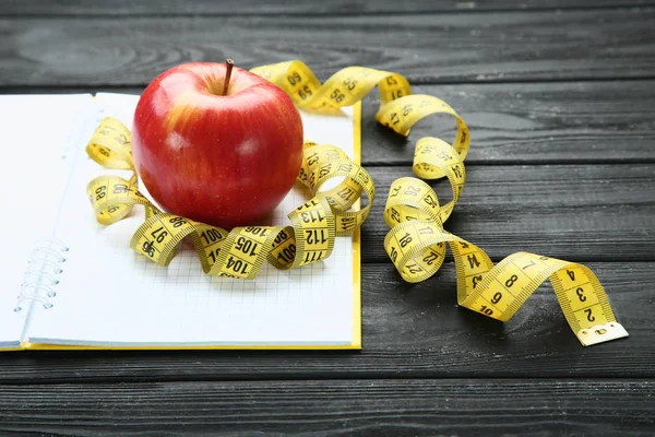 Measuring tape with red apple and notepad on wooden table