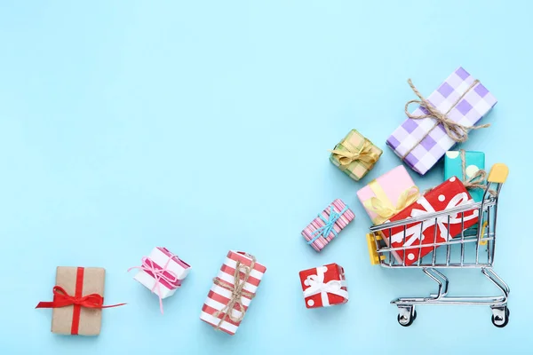 Mavi arka planda hediye kutuları ile küçük alışveriş sepeti — Stok fotoğraf