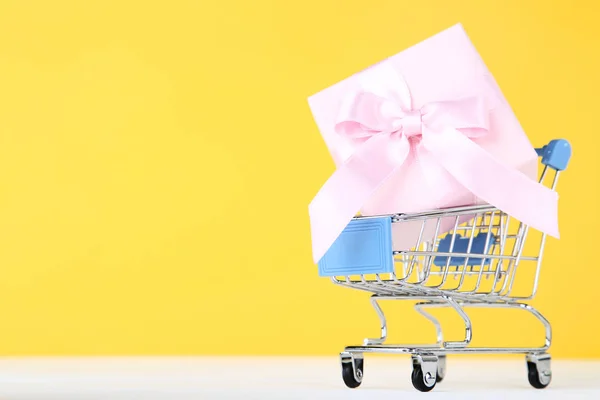 Pequeño carrito de compras con caja de regalo sobre fondo amarillo —  Fotos de Stock