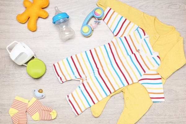 Baby clothes with toys, cup and bottle on the floor — Stock Photo, Image