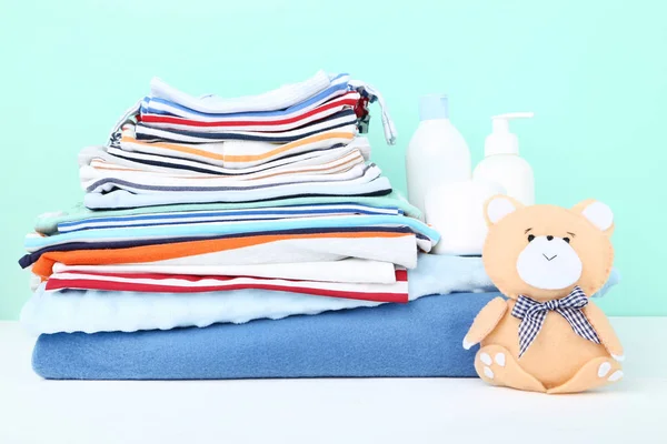 Roupas dobradas com brinquedo de urso macio e suprimentos para bebês — Fotografia de Stock