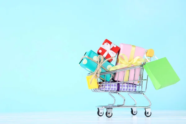 Pequeño carrito con cajas de regalo y bolsa de compras sobre fondo azul —  Fotos de Stock
