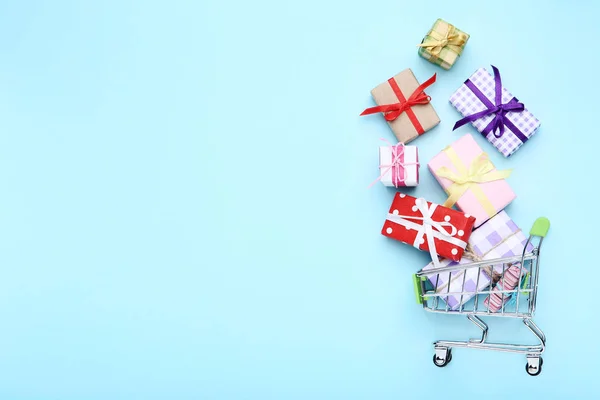Mavi arka planda hediye kutuları ile küçük alışveriş sepeti — Stok fotoğraf