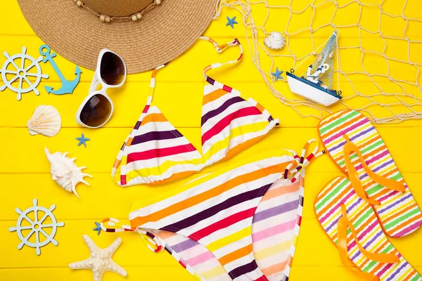 Fashion swimsuit with clothing and seashells on yellow wooden ta — Stock Photo, Image