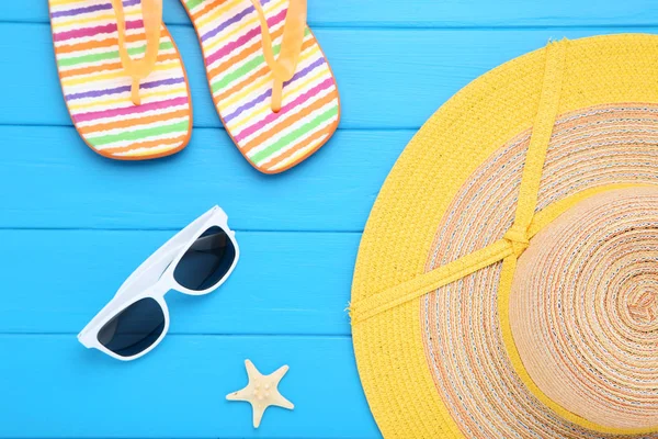 Plážový klobouk s slunečními brýlemi a pantopety na modrém dřevěném stole — Stock fotografie