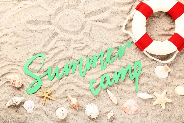 Texto en papel Campamento de verano con conchas marinas y boya salvavidas en arena de playa — Foto de Stock