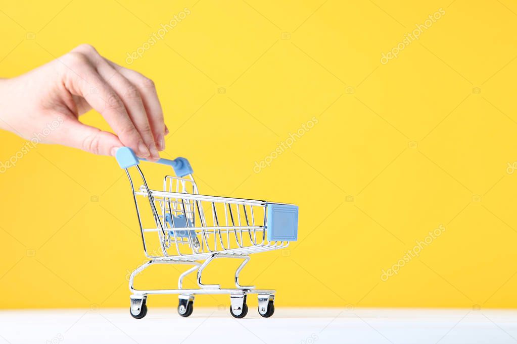 Small shopping cart with female hand on yellow background