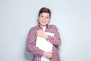 Gri arka planda dizüstü bilgisayar tutan genç bir çocuk.