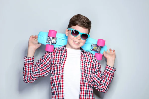 Ung pojke i solglasögon som håller skateboard på grå bakgrund — Stockfoto
