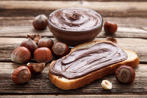 Roti dengan coklat cair dan hazelnut di atas meja kayu cokelat — Stok Foto