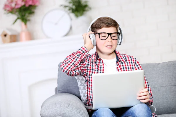 Ung gutt med bærbar PC og hodetelefoner sittende på sofaen – stockfoto