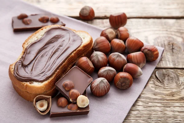 Roti dengan coklat cair dan hazelnut di atas meja kayu — Stok Foto