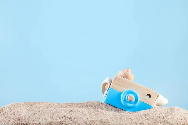 Wooden toy camera in beach sand on blue background — Stock Photo, Image