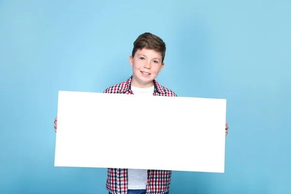 Niño sosteniendo tablero blanco en blanco sobre fondo azul — Foto de Stock