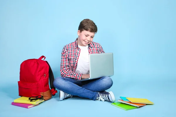 Молодий хлопчик з ноутбуком і книгами сидить на синьому фоні — стокове фото
