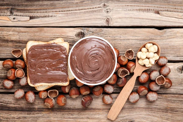 Bread with melted chocolate and hazelnuts on brown wooden table — Stock Photo, Image