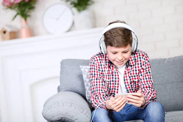 Молодий хлопець з навушниками та смартфоном сидить на дивані — стокове фото