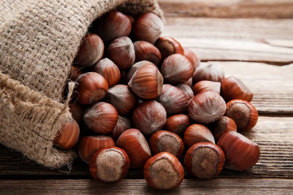 Mogna hasselnötter i säckväv på brunt träbord — Stockfoto