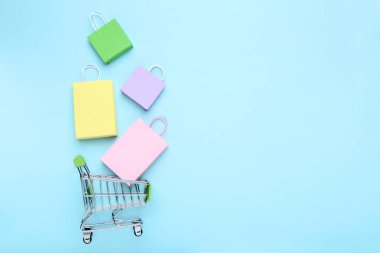 Mavi arka plan üzerinde alışveriş çantaları ile küçük metal sepeti