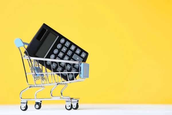 Small shopping cart with calculator on yellow background — Stock Photo, Image