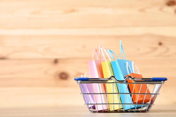 Small metal cart with shopping bags on brown wooden table — Stock Photo, Image