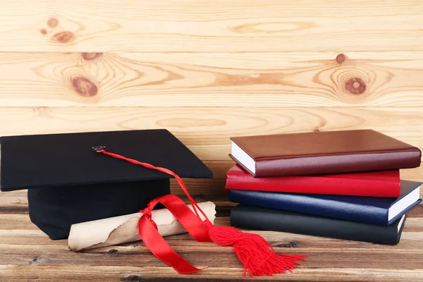 Graduation cap with diploma and stack of books on brown wooden t