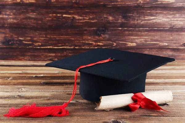 Graduation cap with diploma on brown wooden table — Stock Photo, Image