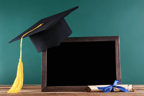 Выпускной колпачок с дипломом и пустой рамой на зеленой доске — стоковое фото