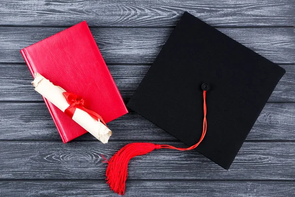 Tapa de graduación con diploma y bloc de notas sobre mesa de madera negra — Foto de Stock