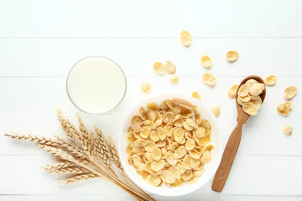 Corn flakes in milk with wheat ears on white wooden table