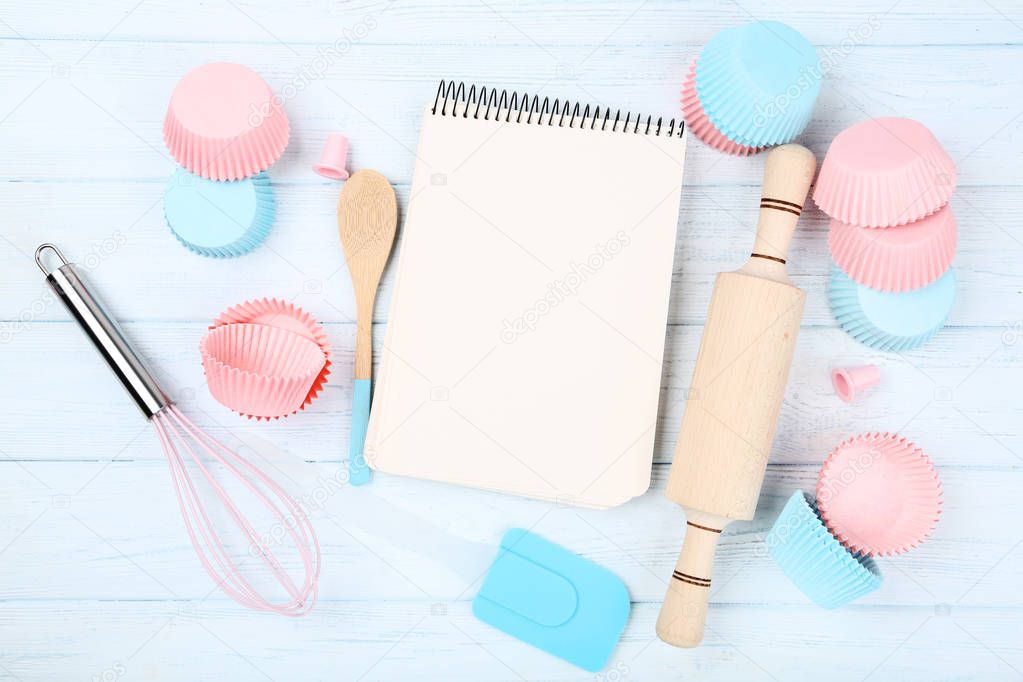 Cupcake cases with kitchen utensils and blank sheet of paper on 
