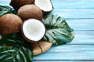 Mavi ahşap masa üzerinde monstera yaprakları ile Olgun hindistan cevizi