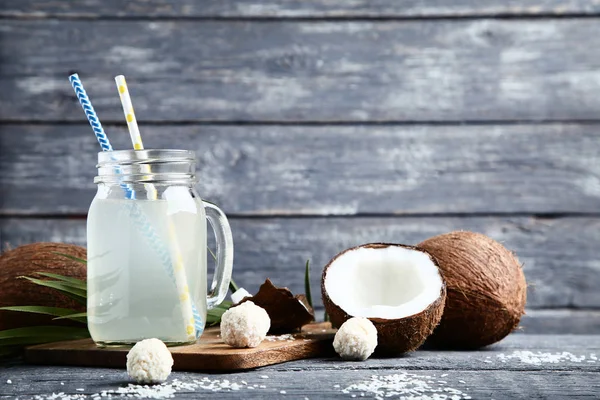 Agua de coco en frasco con caramelos sobre mesa de madera — Foto de Stock