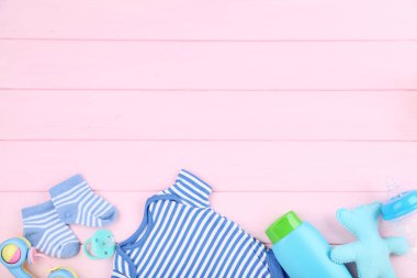 Pembe ahşap masa üzerinde oyuncaklar ve şişe ile bebek giysileri