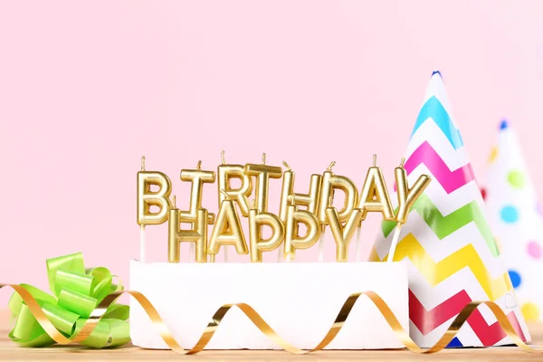 Happy Birthday candles with ribbon and paper cap on pink backgro — Stock Photo, Image