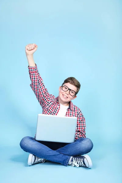 Молодий хлопчик з ноутбуком, що сидить на синьому фоні — стокове фото