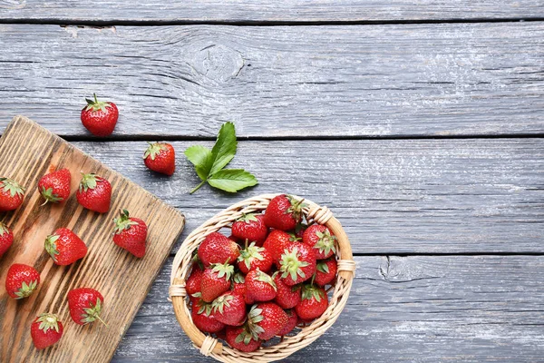 Fresh strawberries in basket with cutting board on grey wooden t — Stock Photo, Image