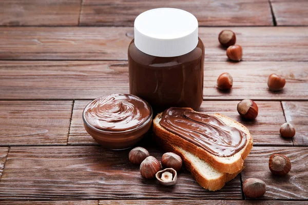 Bröd med smält choklad och hasselnötter på träbord — Stockfoto