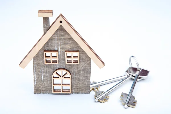 Серебряные ключи с деревянным домом на сером фоне — стоковое фото