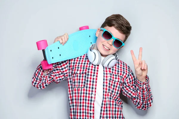 Ung pojke med hörlurar som håller skateboard på grå bakgrund — Stockfoto
