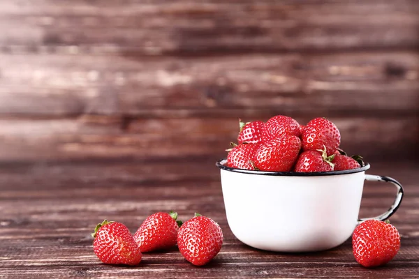 Färska jordgubbar i vit mugg på brunt träbord — Stockfoto