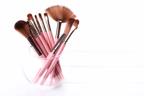 Set de pinceaux de maquillage dans un bol en verre sur une table en bois blanc — Photo