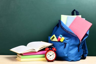 Yeşil arka planda okul malzemeleriyle dolu sırt çantası.