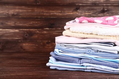 Kahverengi ahşap masada farklı katlanmış bebek kıyafetleri.