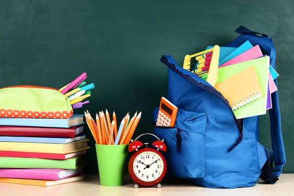 Mochila con útiles escolares sobre fondo verde — Foto de Stock