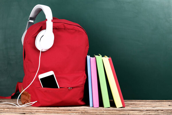 School backpack with headphones, smartphone and books on brown w